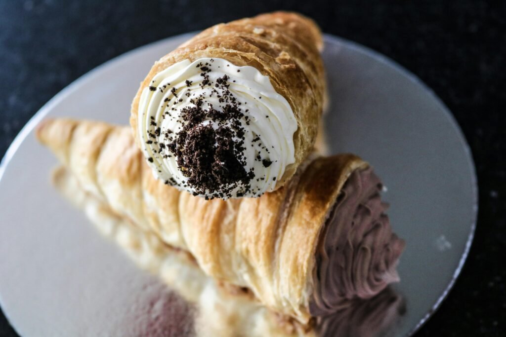 Close-up of two decadent cream-filled pastries on a reflective silver plate, highlighting chocolate and vanilla flavors.